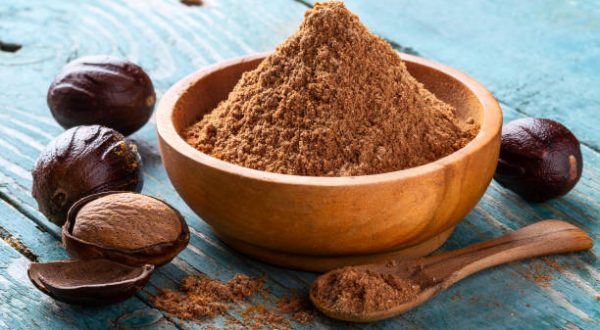 Whole inshell nut, cracked and nutmeg powder in a wooden bowl and spoon on old blue rustic background close-up. indian spice.