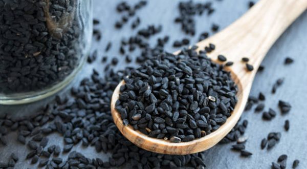 Black cumin seeds on a wooden spoon on gray background
